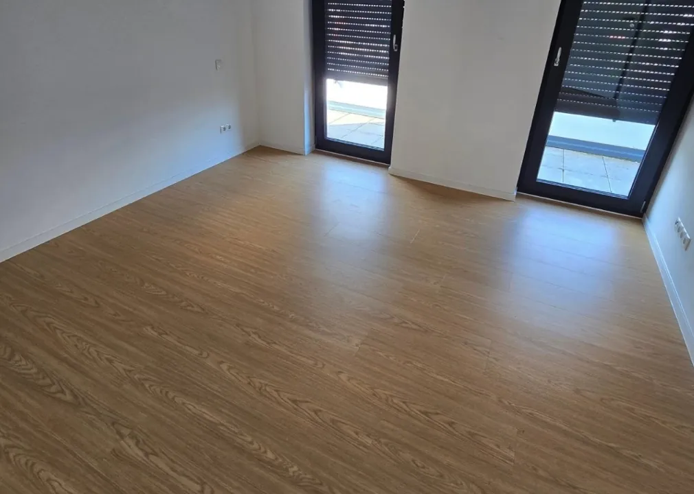 Neues Laminat in modernem Wohnraum - Verlegung von neuem Laminatboden in Holzoptik in einem frisch renovierten Innenraum mit weißen Wänden.